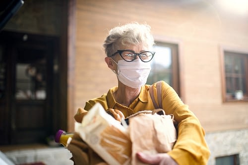 elderly woman in mask holding groceries